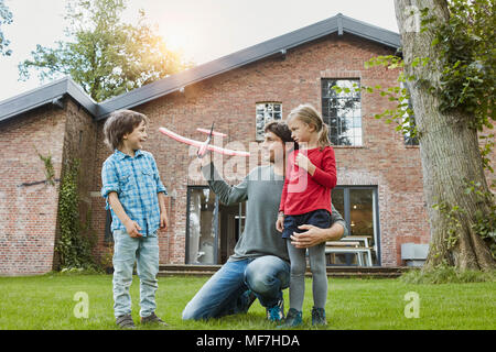 Father with two children playing with toy airplane in garden of their home Stock Photo