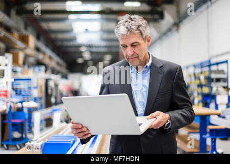Businessman using laptop in production hall Stock Photo