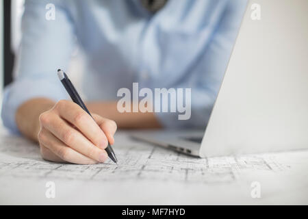 Close-up of man with laptop making notes on plan in office Stock Photo
