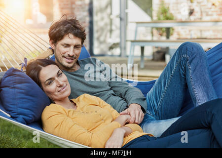 Smiling couple lying in hammock in garden of their home Stock Photo