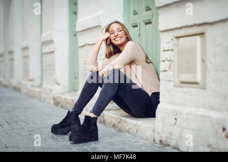 Laughing young woman sitting on step in front of an entrance door Stock Photo
