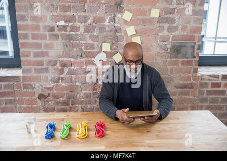Businessman with tablet and coloured power cables at wooden table Stock Photo