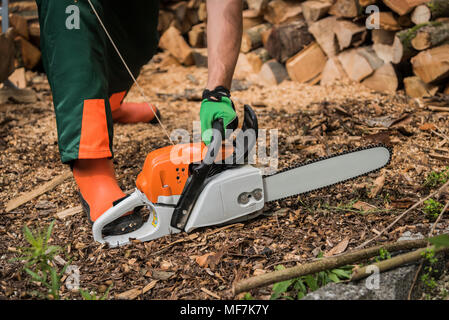 Man wearing protective clothes starting motor saw Stock Photo