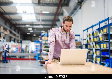 Young businessman using laptop in production hall Stock Photo