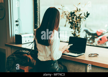Back view of businesswoman using laptop and cell phone in a coffee shop Stock Photo