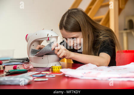 Smiling girl using sewing machine Stock Photo
