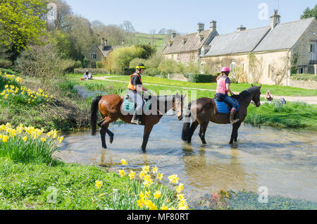 Horses crossing the River Eye through a ford in the pretty Cotswold village of Upper Slaughter in Gloucestershire,UK Stock Photo