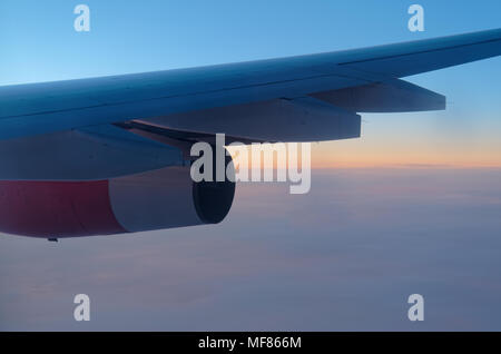 Airplane wing and turbine over clouds and blue sky at sunset Stock Photo