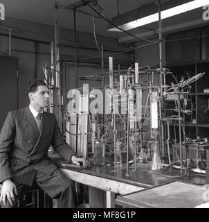 1948, historical, young male research scientist wearing a pin-stripe suit sitting next to the elaborate apparatus of pipes, tubes and glass bottles built for his research into the chemical properties of coal and carbon monoxide in a laboratory in the Dept of Coal, Gas, and Fuel Industries at Leeds University. Stock Photo