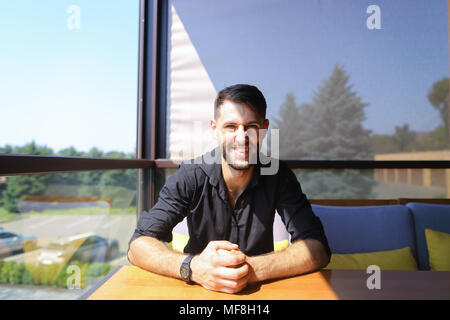 Male manager sitting at table on sofa and smiling, wearing black shirt. Stock Photo