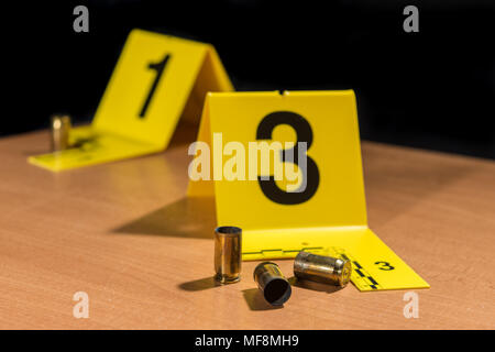 Expended bullet casings on a wood surface marked by crime scene evidence markers. Stock Photo