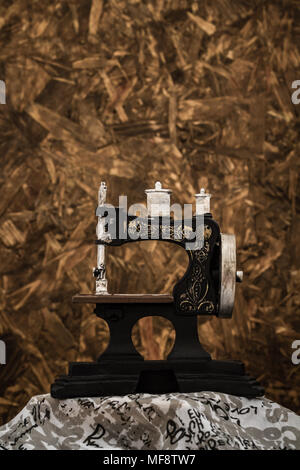Small nostalgic decorative sewing machine on brown wooden background Stock Photo