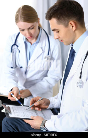 Doctors writing papers using clipboard. Physicians discussing medication program or studying at medical conference. Healthcare, insurance and medicine concept Stock Photo