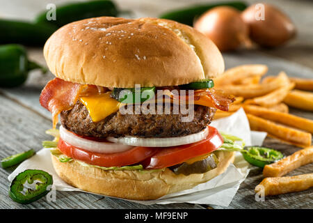 A delicious burger with bacon, cheddar, jalapeno pepper, tomato, onion, pickle and lettuce with french fries. Stock Photo