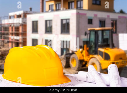 Helmet and blueprints and a construction site with wheel loader in the background Stock Photo