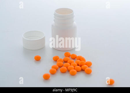 orange tablets spilled out of the plastic bottle and lie next to each other. The bottle is open Stock Photo