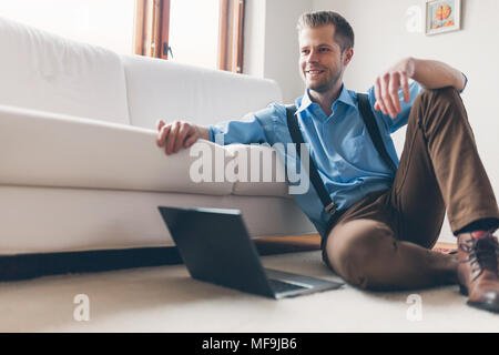 Handsome man at home in the living room using his laptop Stock Photo