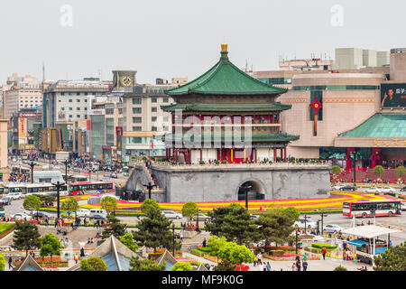 Xi'an Bell Tower with it's ornate green tiled roof stands in the middle of a busy traffic island. Behind it some of the many shopping malls. Stock Photo