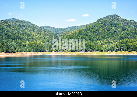 Daylight view to Vidraru lake in Carpathian Mountains. Bright blue sky and green trees. Negative copy space, place for text. Transfagarasan, Romania Stock Photo