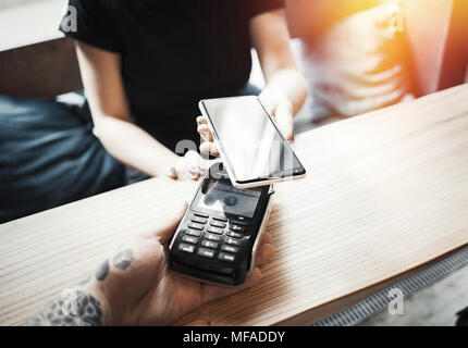 Young woman pays via payment terminal and mobile phone. Stock Photo