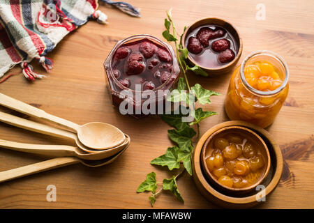 Various glass bowl of Fruit jams Apricot, cherry, strawberry, damson plum in wooden tray. Stock Photo