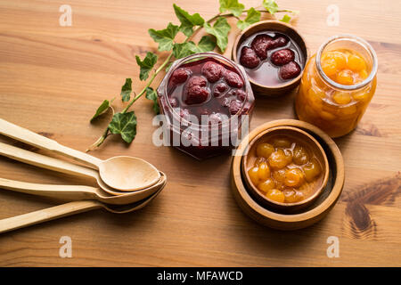 Various glass bowl of Fruit jams Apricot, cherry, strawberry, damson plum in wooden tray. Stock Photo