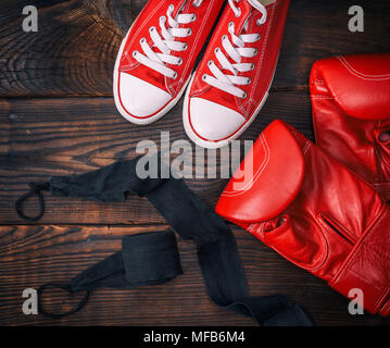red leather boxing gloves and textile sneakers on a brown wooden background, top view Stock Photo