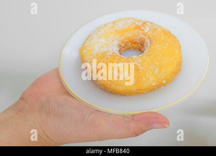 Food and Bakery, Hand Holding Delicious Fresh and Sweet Donut with Sugar Toppings on White Dish. Stock Photo