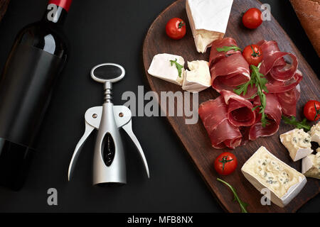 Wine bottle with cheese and traditional sausages on wooden board on black background with copy space Stock Photo