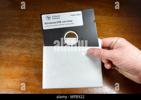 A 5¼-inch floppy disk being held in the right hand of a man with a table behind. Stock Photo