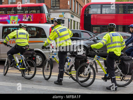 Three metropolitan police officers and community support officers on cycles or bicycles riding through the traffic on the beat in the centre of london Stock Photo