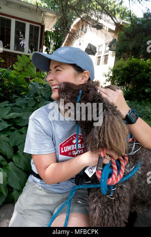 Woman being nuzzled by her pet labradoodle crossbreed dog during a rest break on a neighborhood walk. St Paul Minnesota MN USA Stock Photo