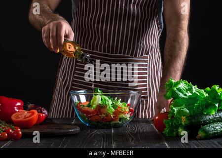 Cooking and home concept - close up of male hands flavouring salad in a bowl with olive oil Stock Photo