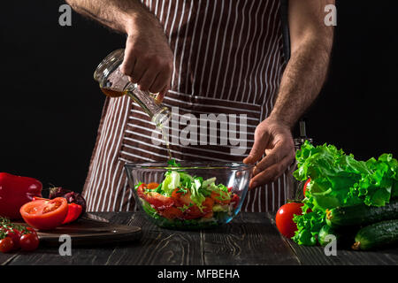 Cooking and home concept - close up of male hands flavouring salad in a bowl with olive oil Stock Photo