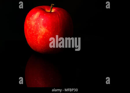 A red apple with water drops on skin isolated on black background with copy space. Healthy fruit and healthy food concept. Vegan food. Stock Photo