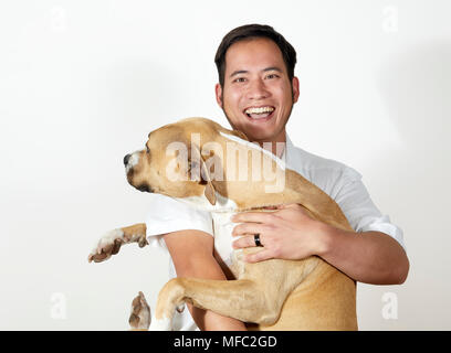 Young Adult man laughing while holding a medium to large size dog in his arms isolated on white Stock Photo