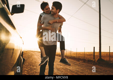 Woman piggy riding on a man outdoors in country side. Man carrying a woman on his back while on a road trip. Stock Photo