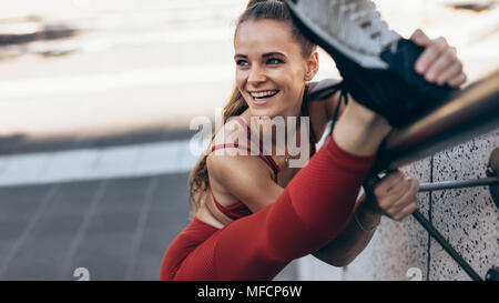 Fit sportswoman doing leg stretches on a railing. Female athlete doing warm up stretches outdoors. Stock Photo