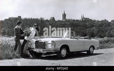 A young couple posing in the grass next to a Mercedes Benz 280 SE 3.5 Cabriolet. (Recording from 1969). | usage worldwide