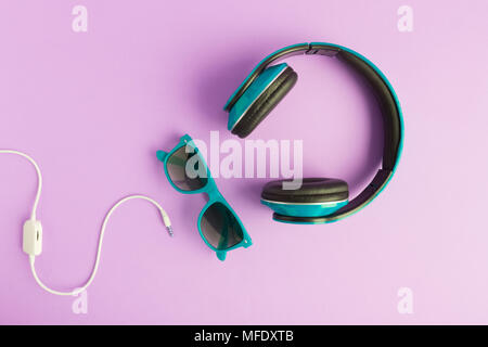 Turquoise headphones and sunglasses with cable isolated on pastel purple background flat lay. Stock Photo