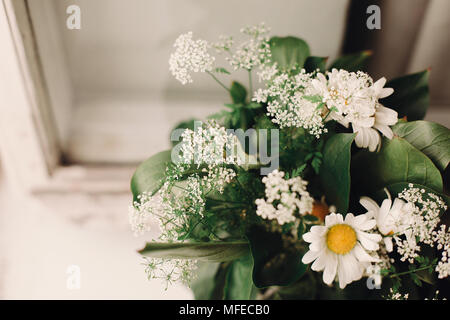 anise and chamomile bouquet in light at rustic white wooden window in light, space for text. daisy and pimpinella wildflowers at country rural place.  Stock Photo