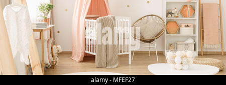 Gold armchair next to a white crib with blanket in pink baby's bedroom interior with ladder Stock Photo