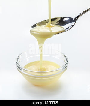 closeup pouring condensed milk with teaspoon on white background Stock Photo