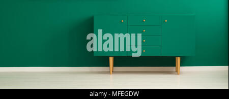 Panorama of a minimalist, green living room interior with a modern, teal sideboard with drawers and wooden legs Stock Photo