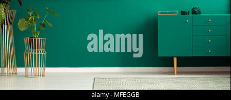 Panorama of a luxurious apartment interior with green walls, golden plant stands and a modern teal sideboard Stock Photo