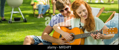 Man teaching his girlfriend how to play guitar during grill party Stock Photo