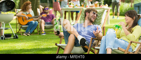 Boy and girl laughing and telling jokes during grill party Stock Photo