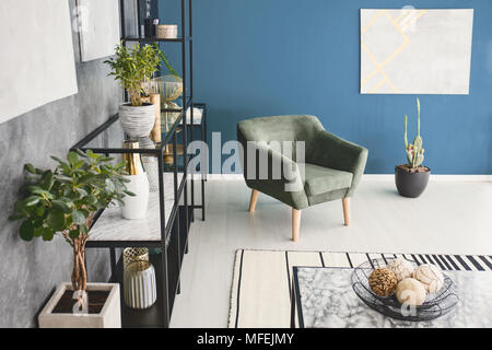 Top view photo of living room interior with green armchair, plants and decor on metal rack and modern painting on the wall Stock Photo