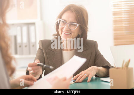 Smiling personal health coach sitting in an office and talking to a woman Stock Photo