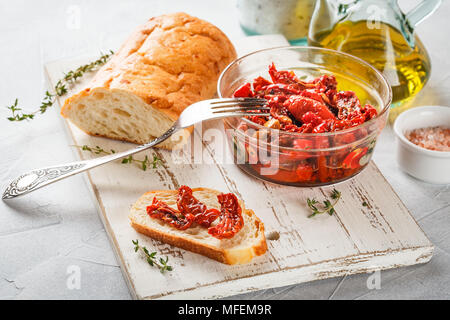 Sun dried tomatoes in glass jar on white cutting board on light background Stock Photo